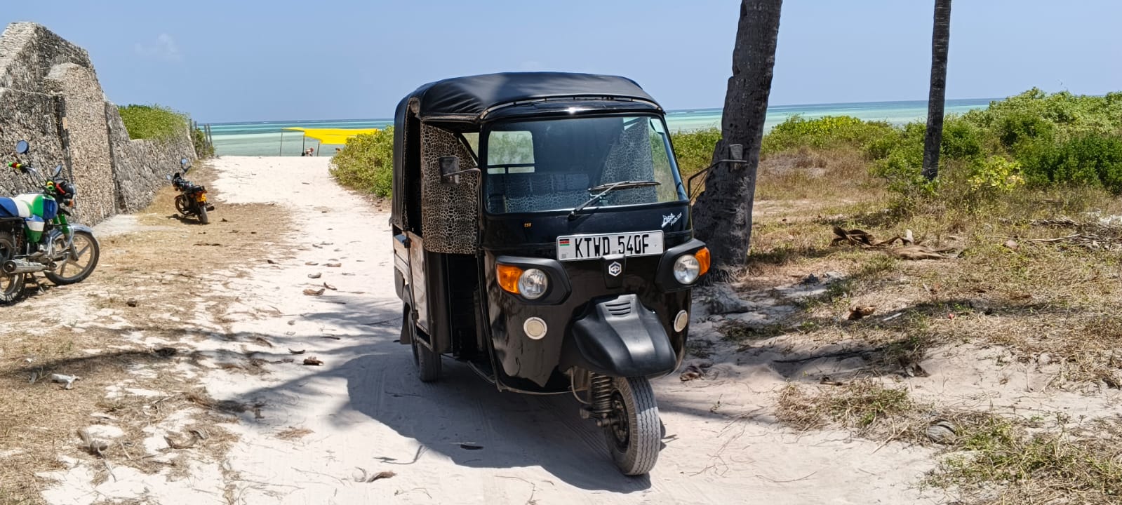 Black tuk tuk parked at the end of a sandy path by Watamu beach